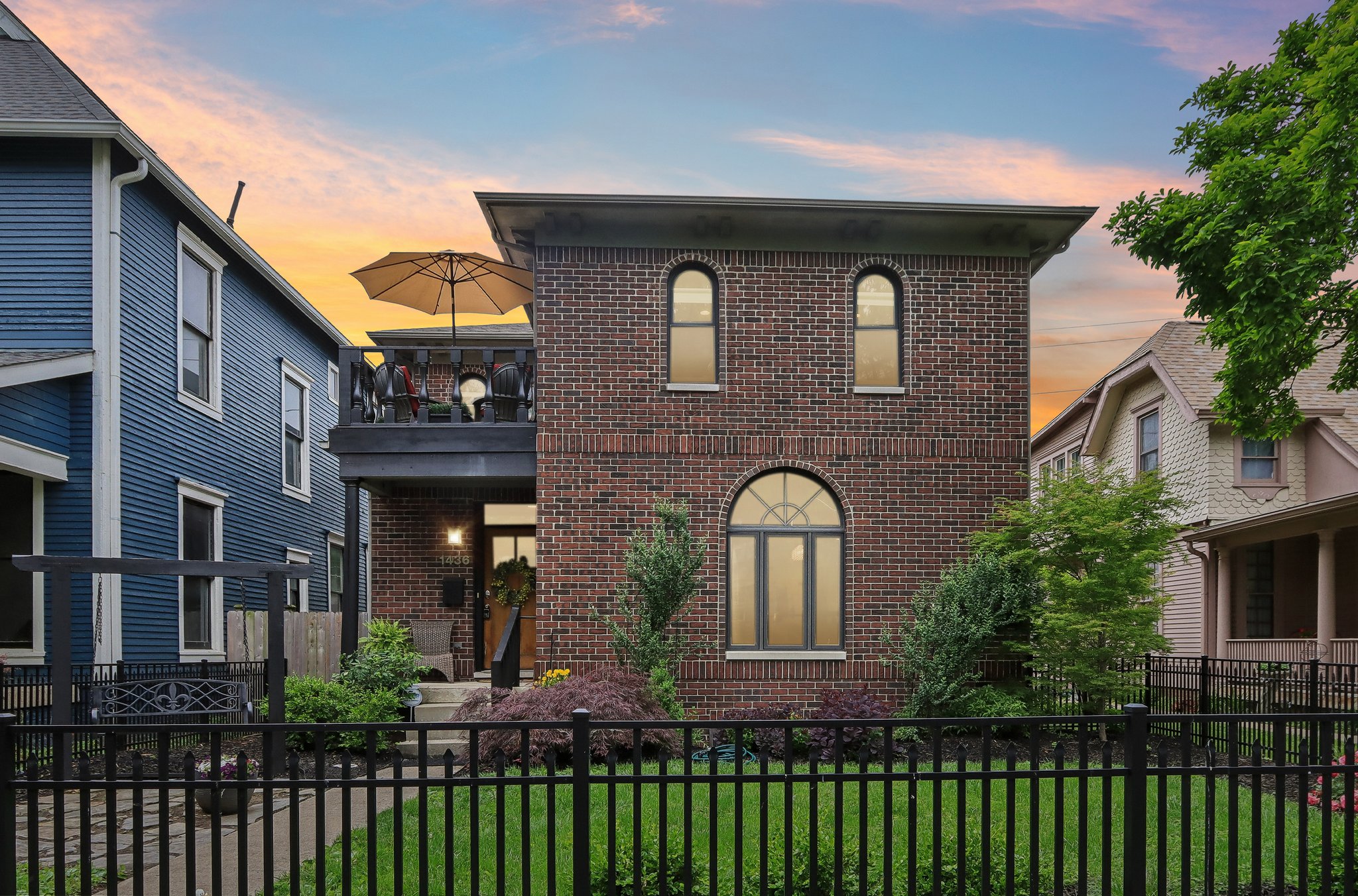 Front of home picture of a two story brick home with a black fence surrounding front yard.